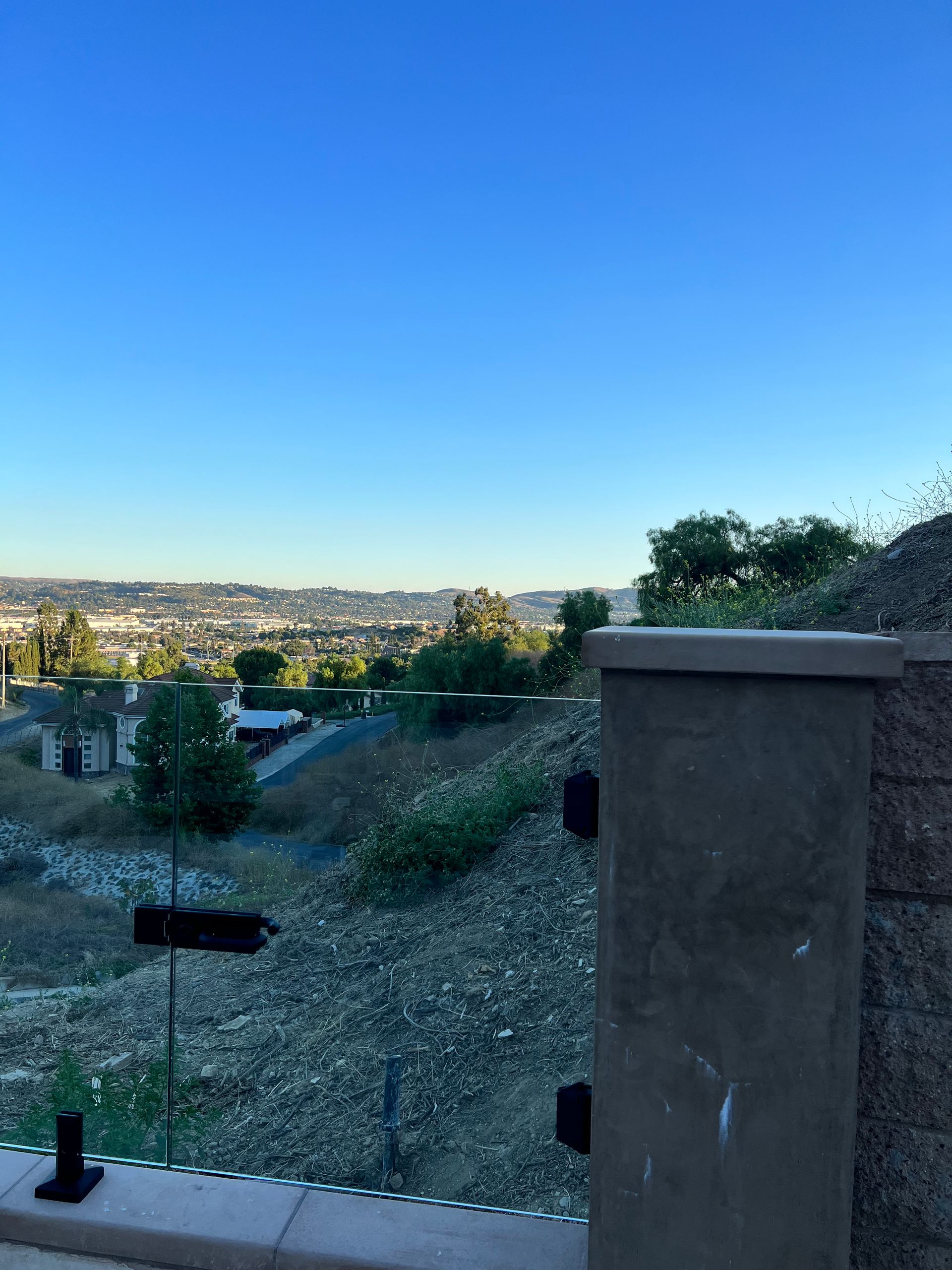 View of a city landscape from a hillside with a concrete barrier and clear blue sky.
