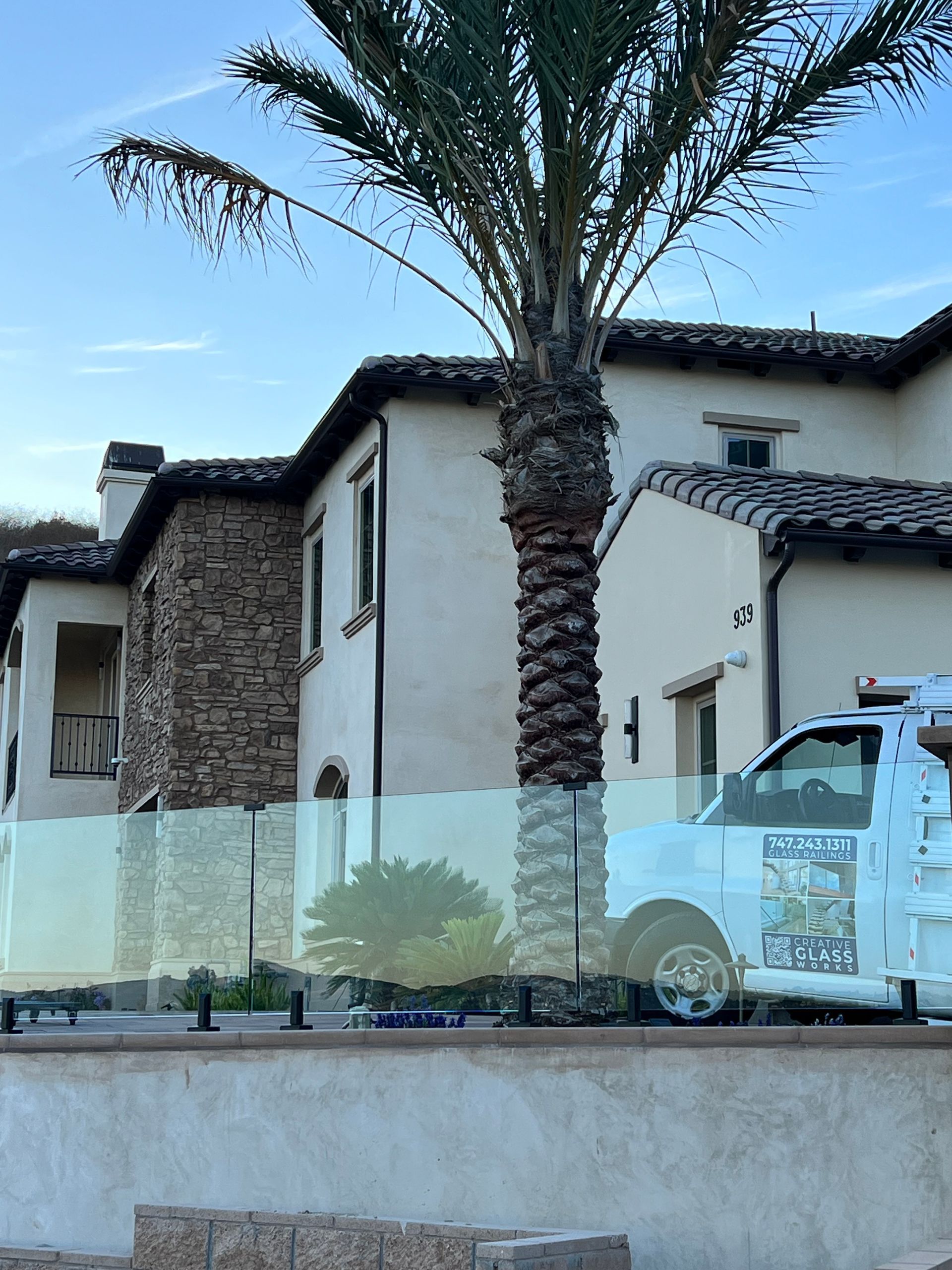 Large house with stone and stucco facade, palm tree, and a white service truck parked nearby.