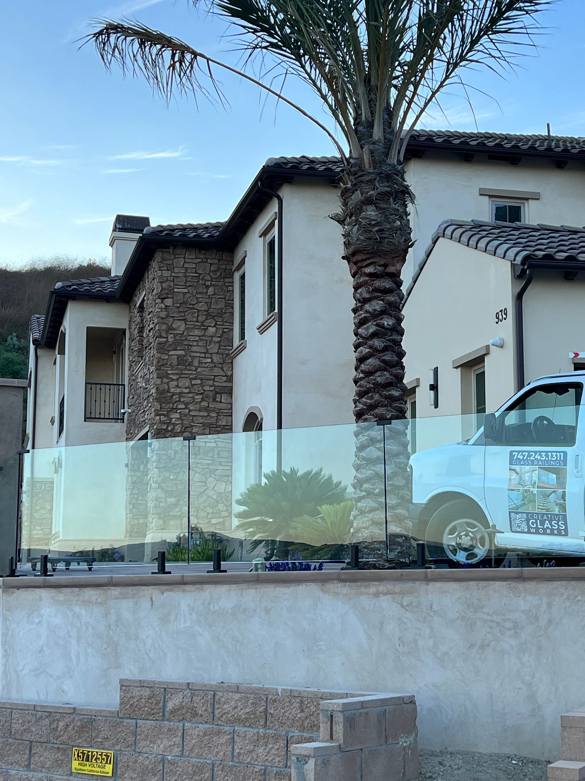 House with glass fence, stone accents, and a palm tree. A white van is partially visible.
