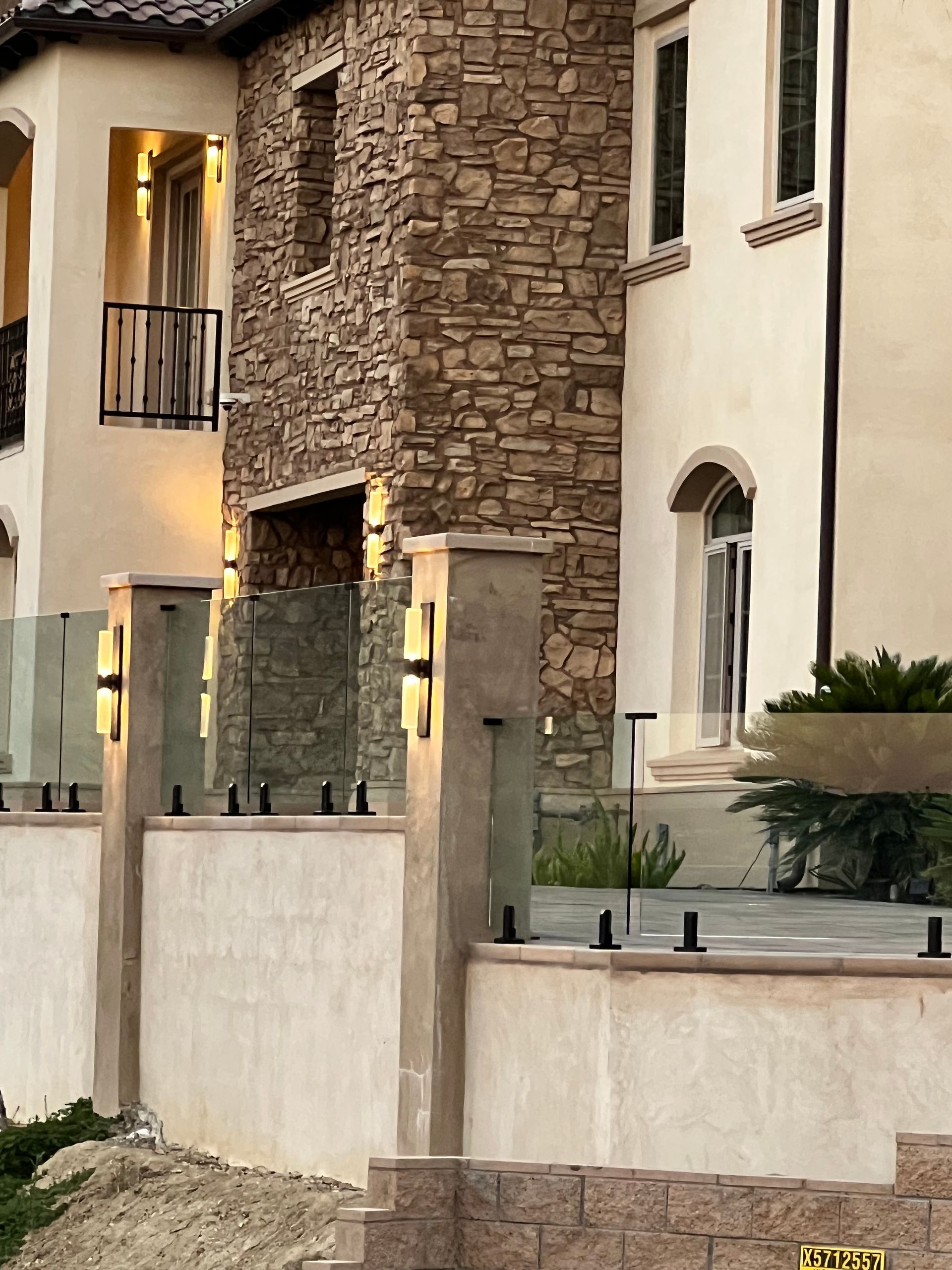 Exterior of a two-story home with stone and stucco facade. Glass railing with black accents.