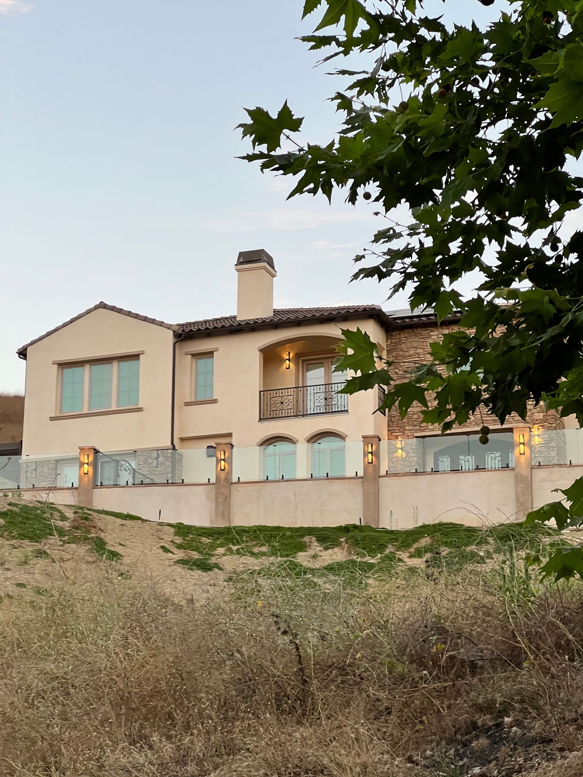 Beige stucco house with glass railing and trees.