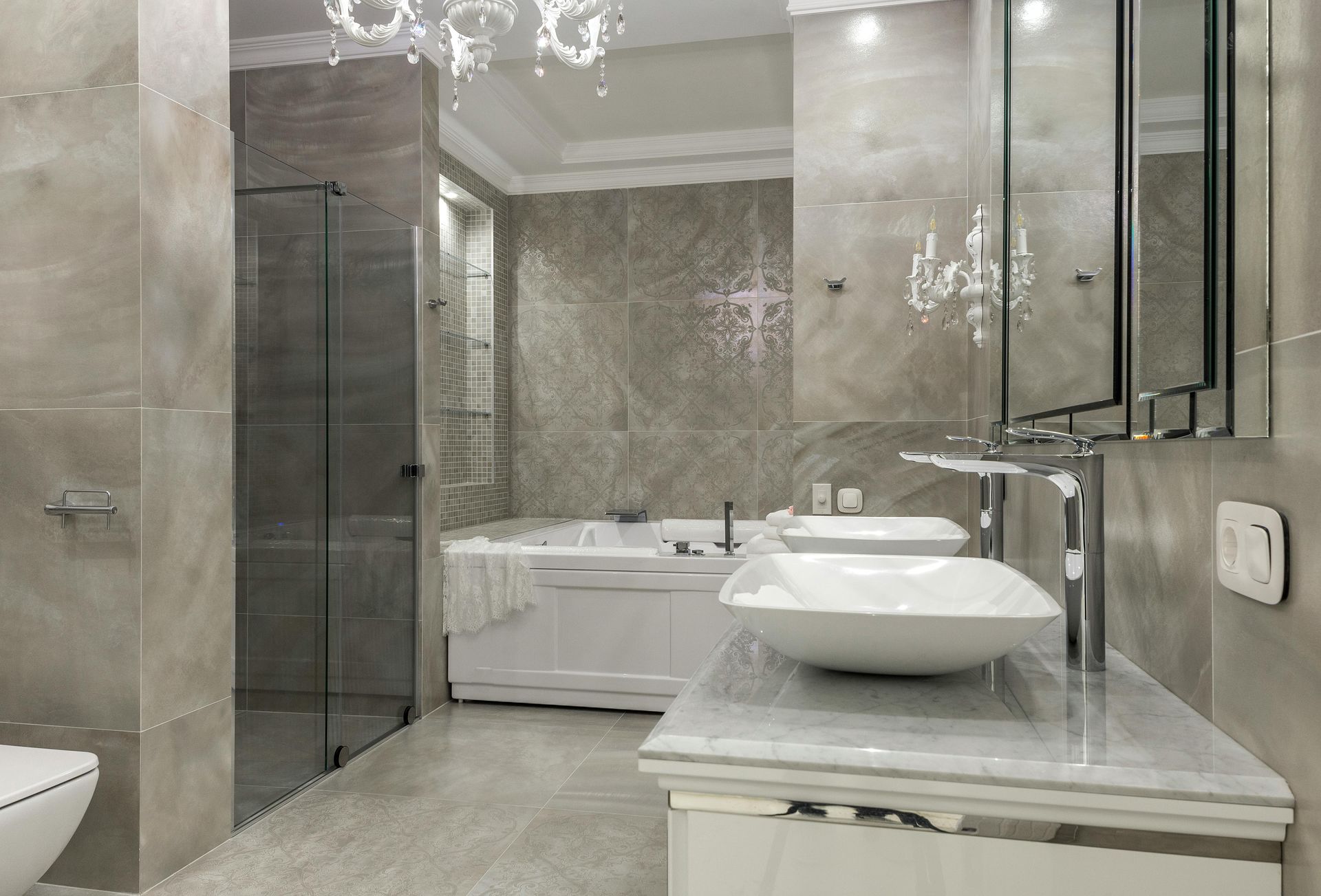 Modern gray bathroom with shower, tub, double sinks, and chandelier.
