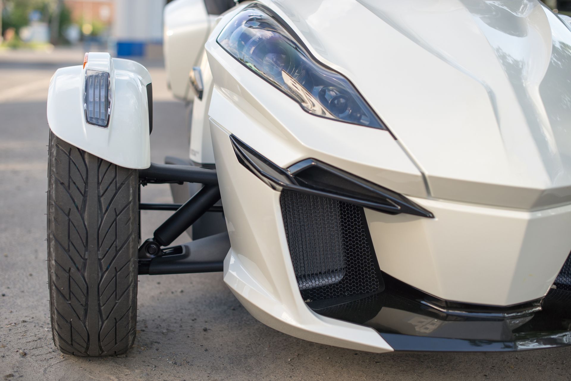 Une moto blanche à trois roues est garée sur le bord de la route.