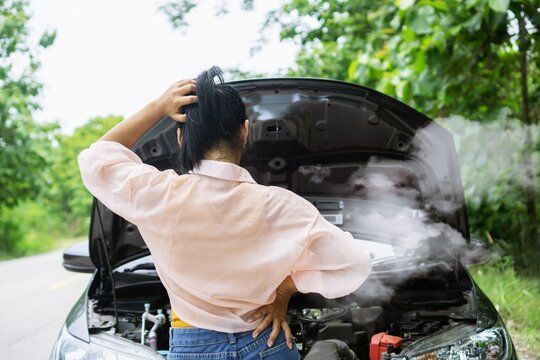 A woman is standing next to a broken down car with the hood open. | Superior Transmissions & Auto