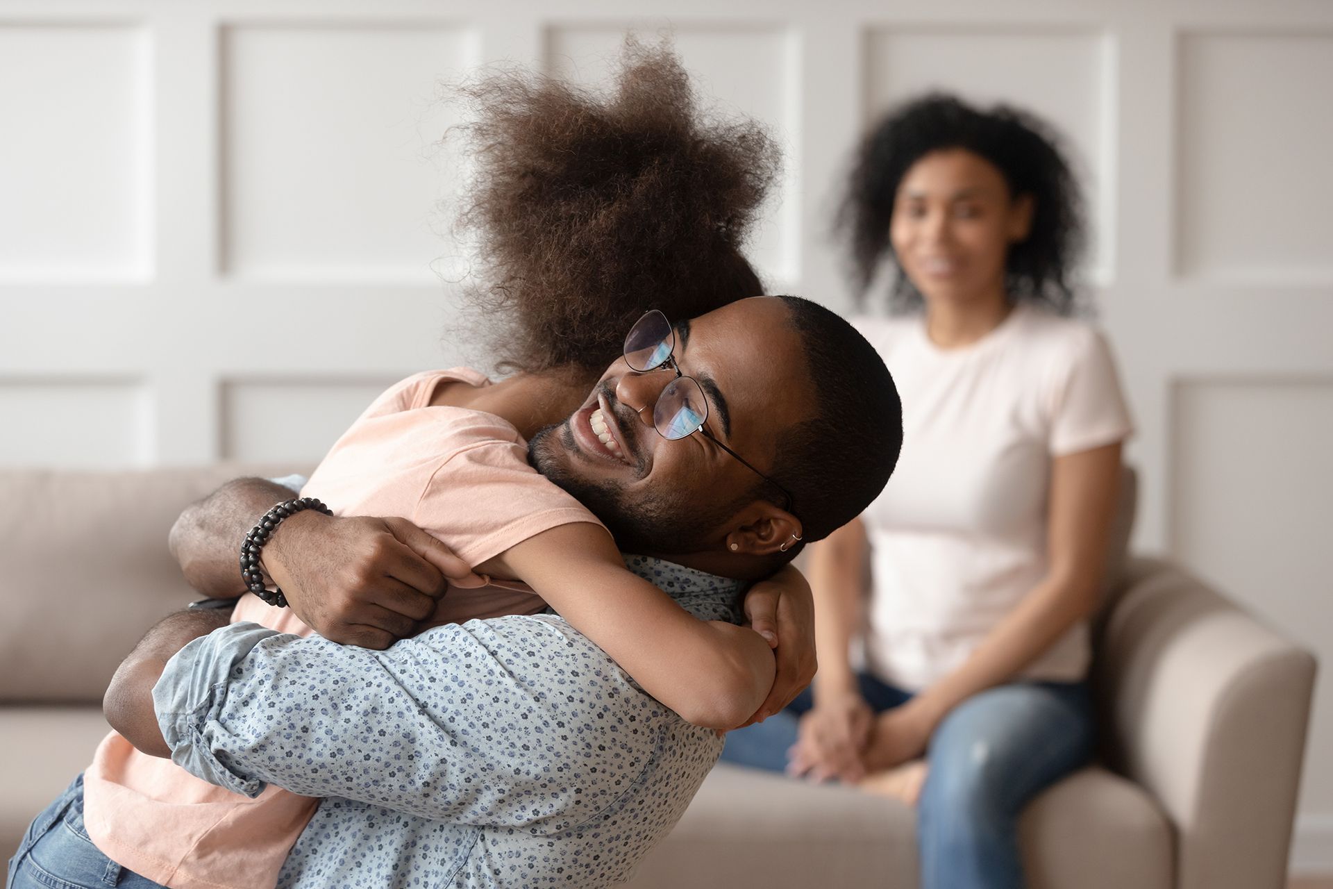 A man is holding a little girl in his arms while a woman sits on a couch.