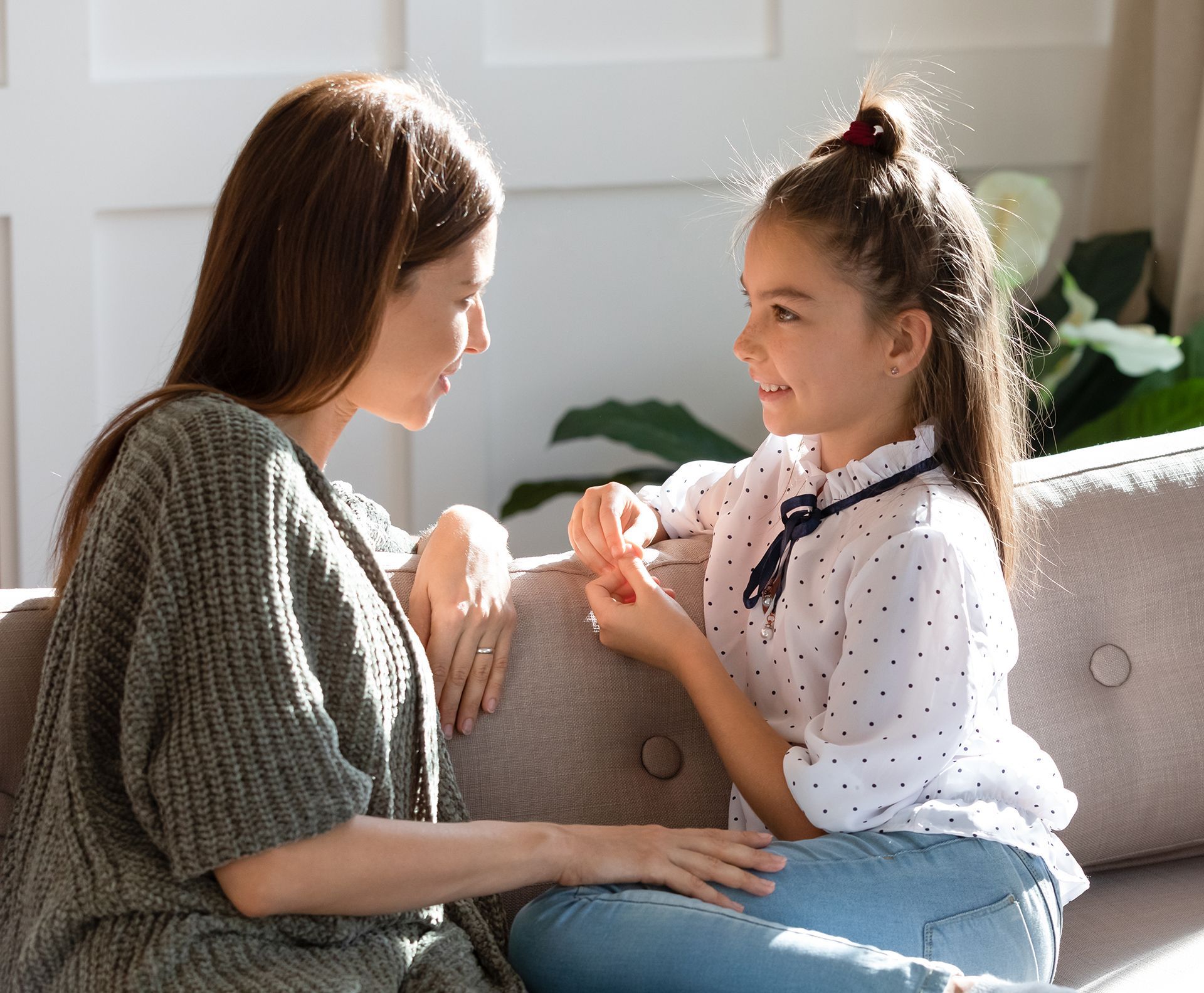 A woman and a little girl are sitting on a couch talking to each other.