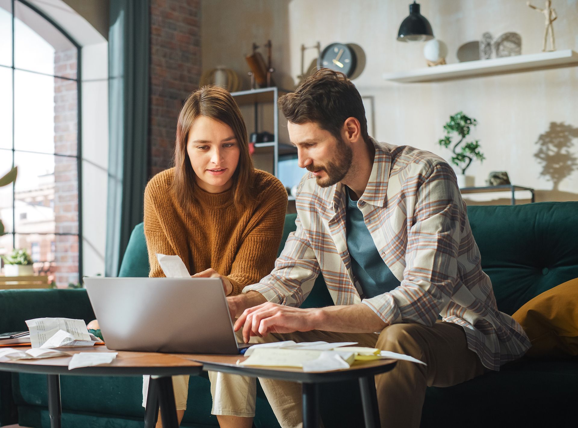 A man and a woman are sitting on a couch looking at a laptop.