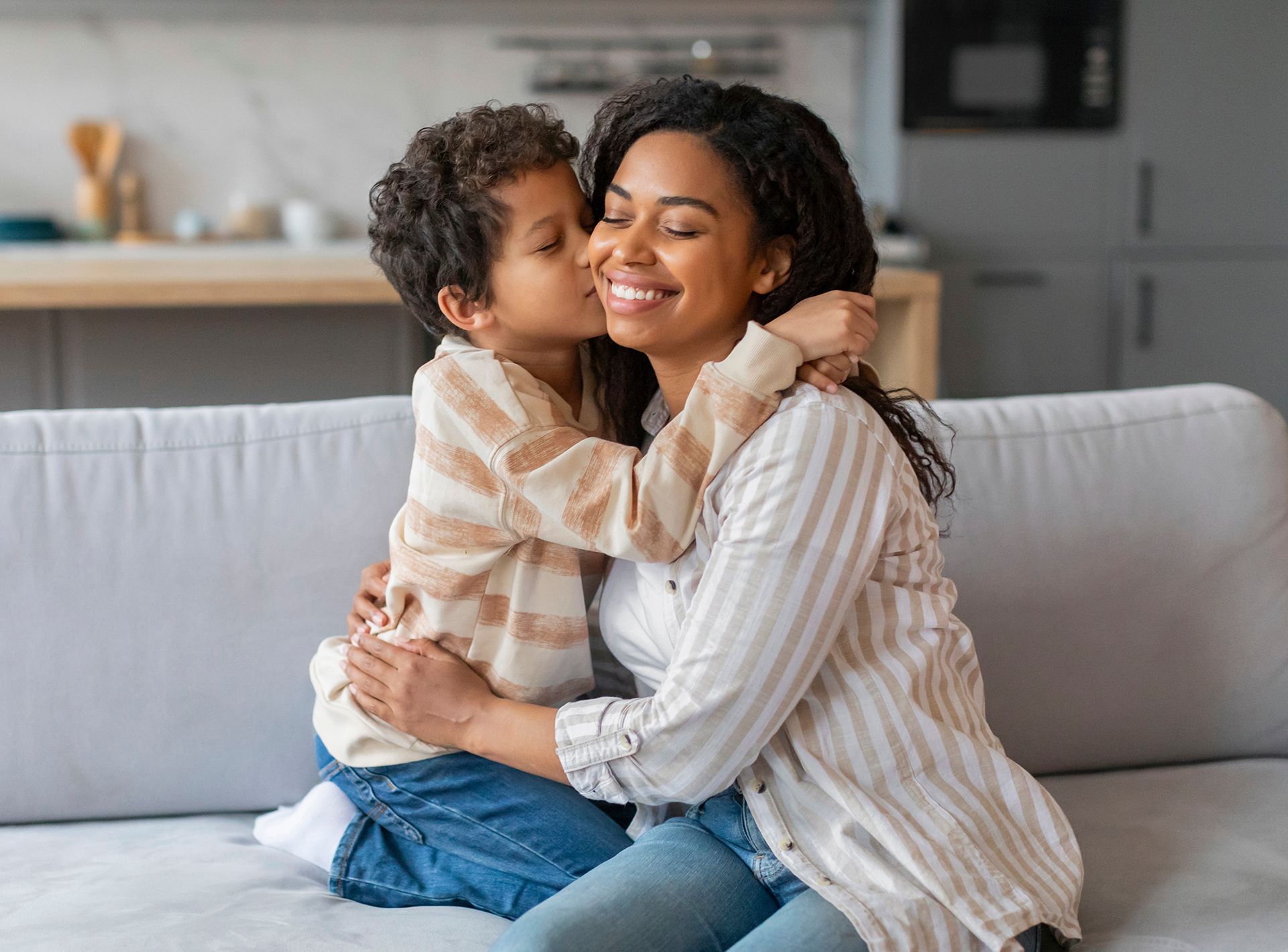 A little boy is kissing his mother on the cheek while sitting on a couch.