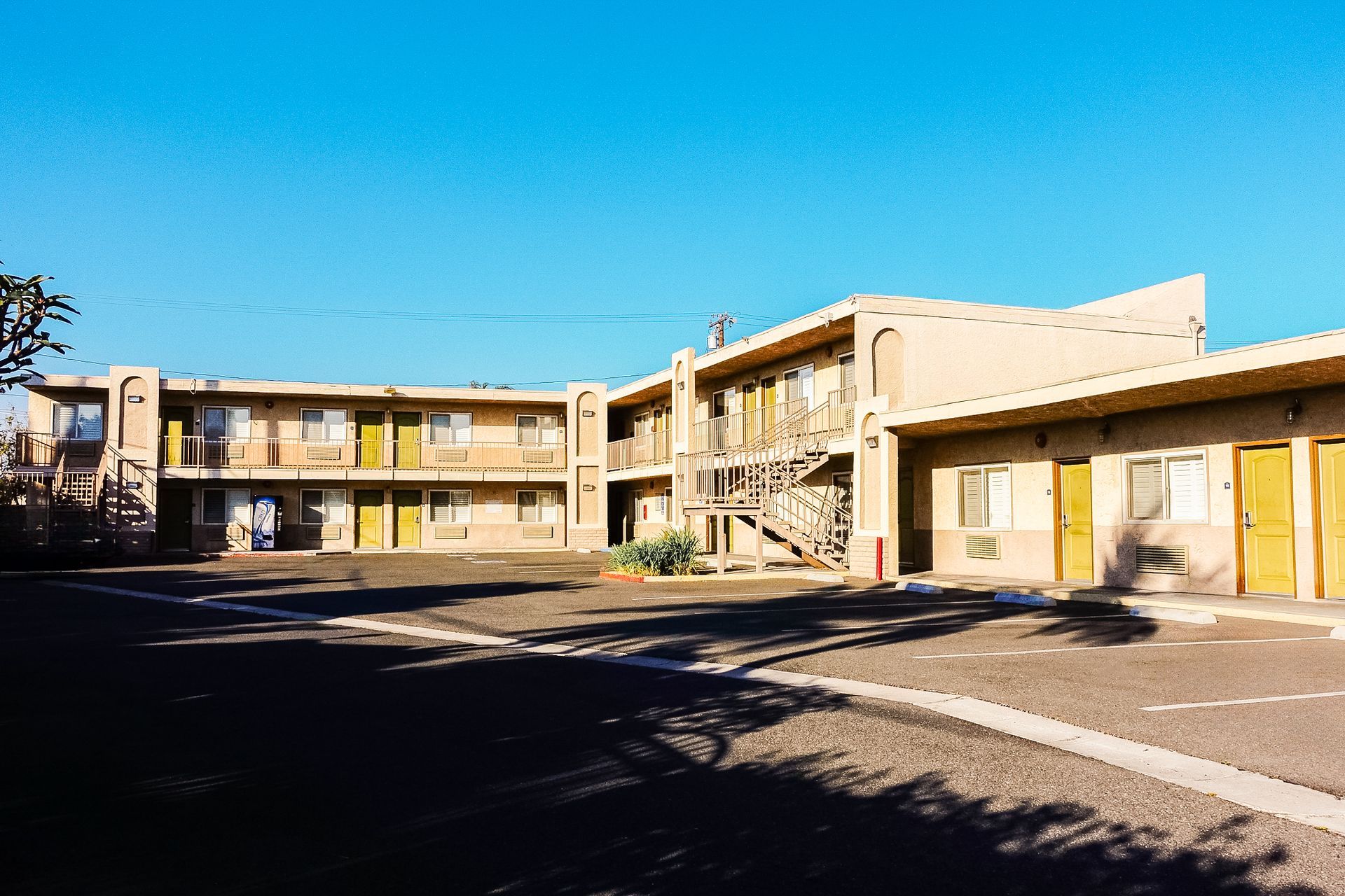 Tan two-story motel with yellow doors and fire escape under a bright blue sky.