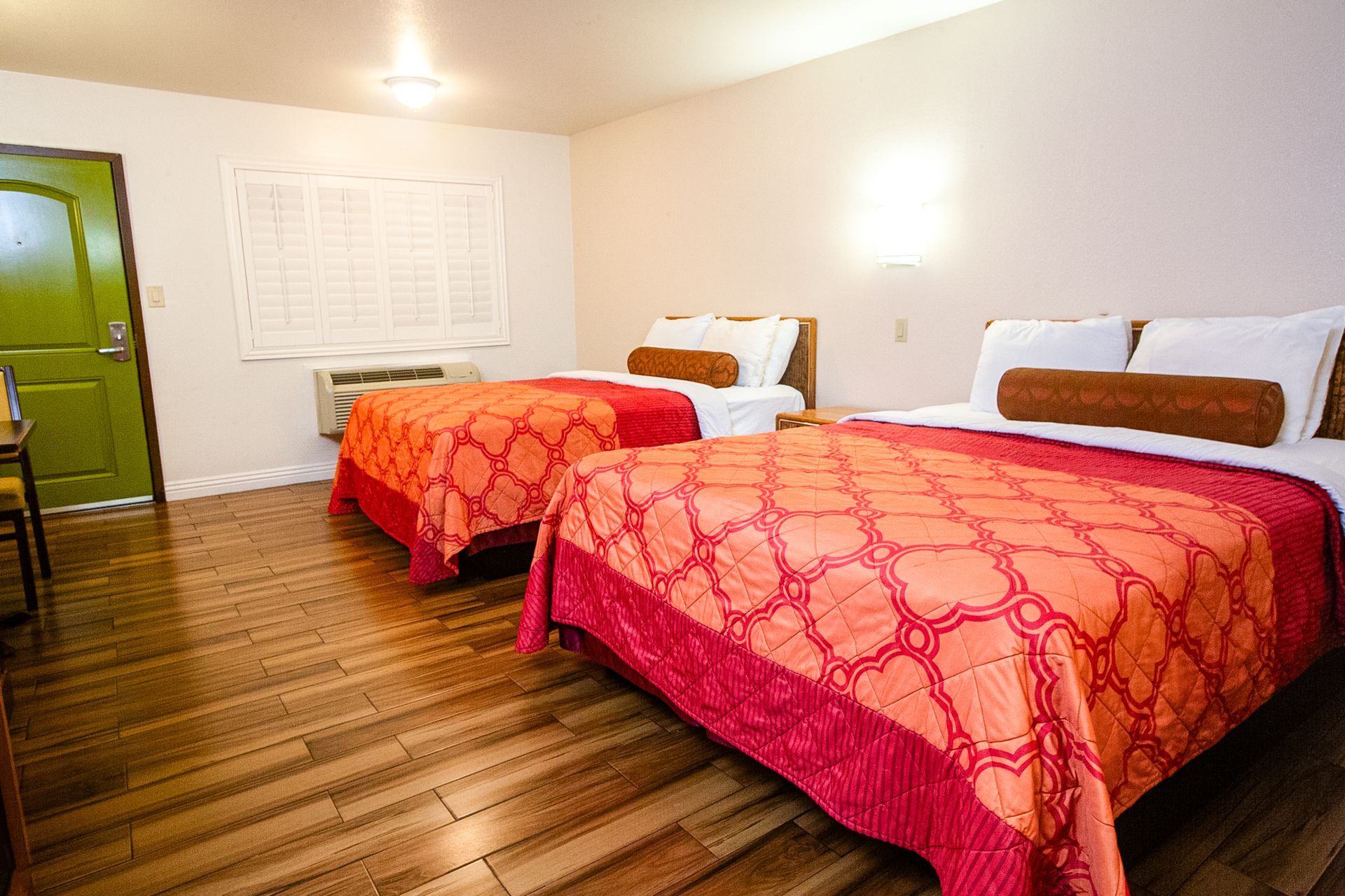 Two beds with orange patterned bedding in a hotel room with wood floors and a green door.