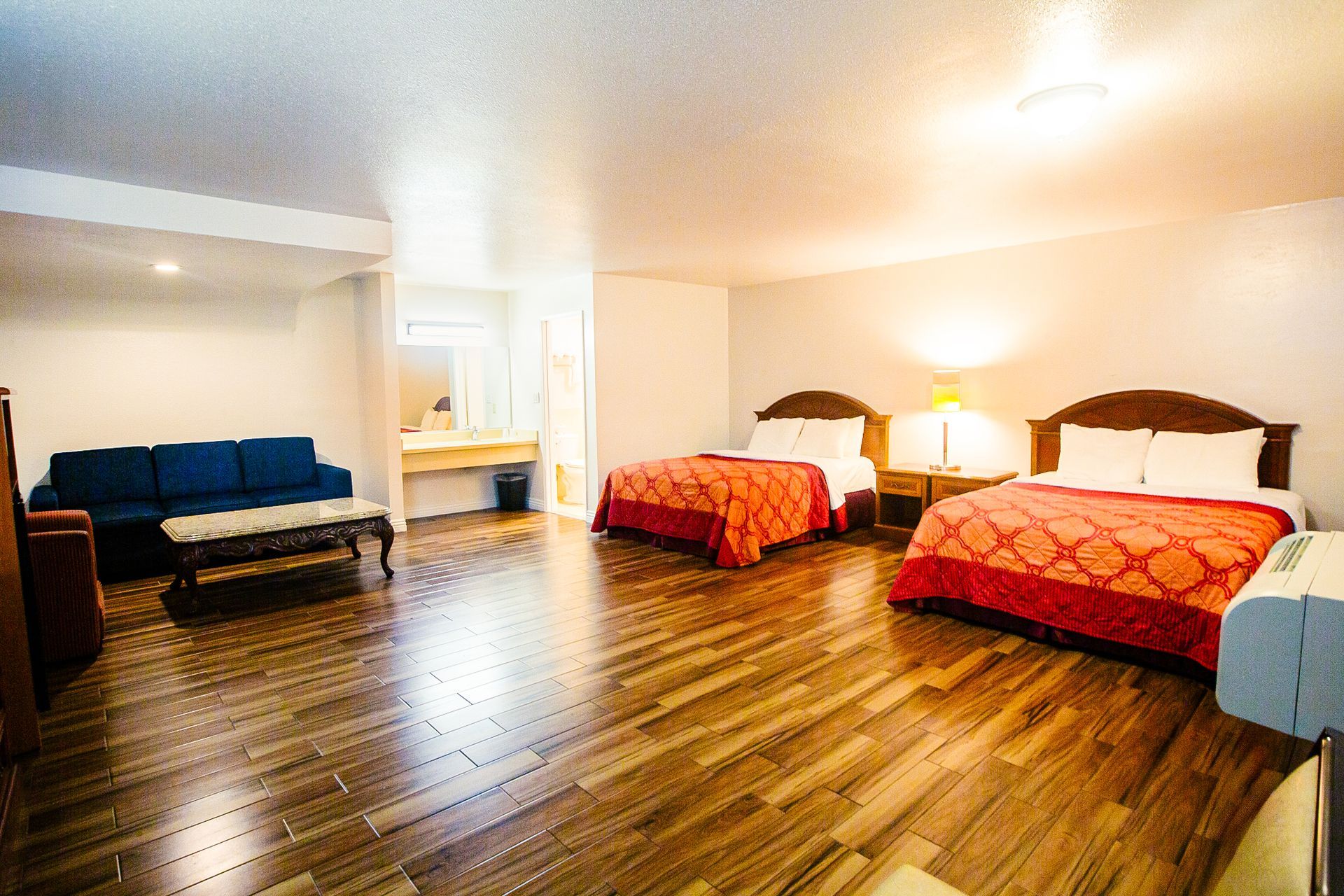 Spacious hotel room with two beds, sofa, and hardwood floors.