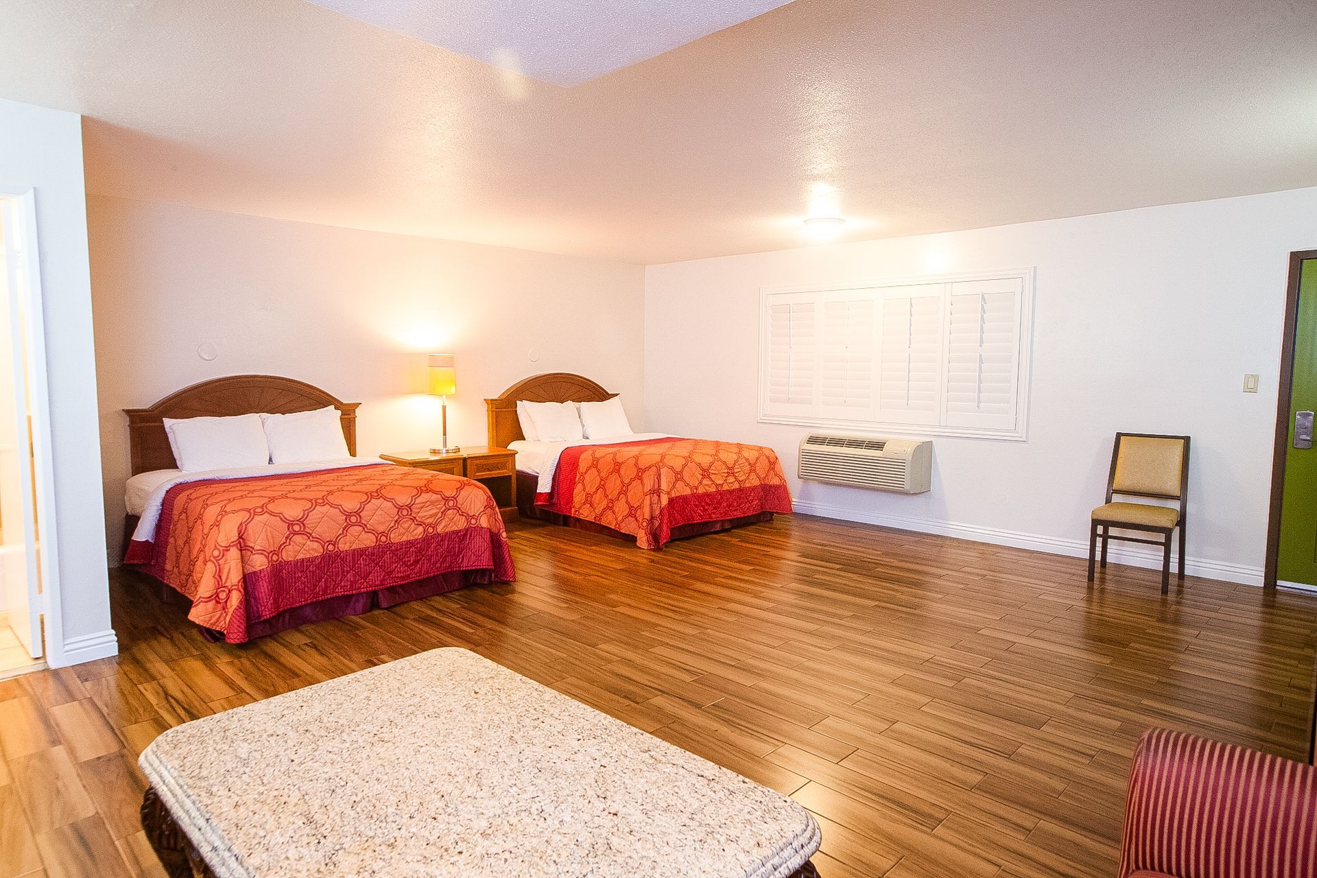 Two double beds in a motel room, with red bedspreads, wooden floors, and a small chair.