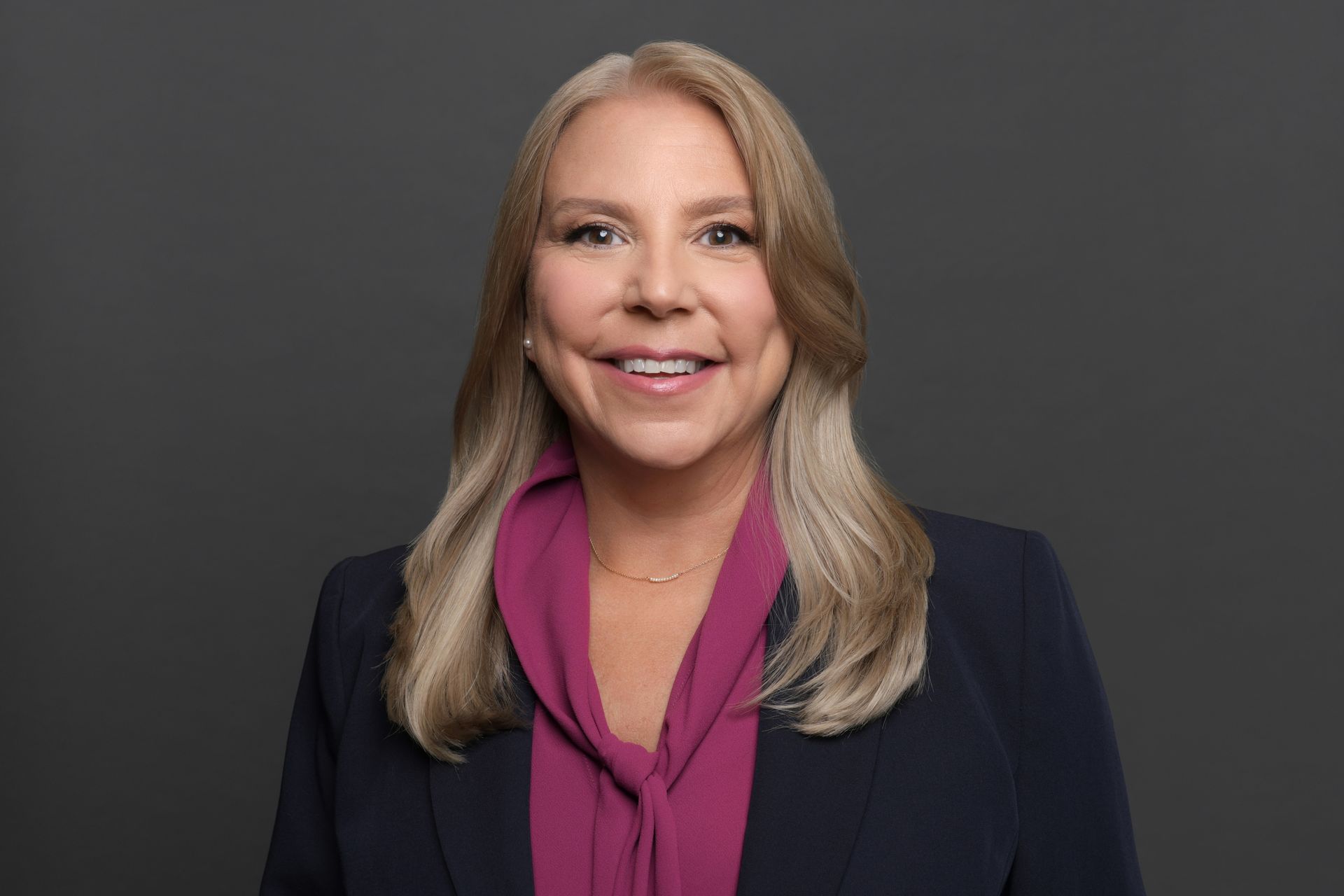 A woman in a blue jacket and a purple shirt is smiling for the camera.