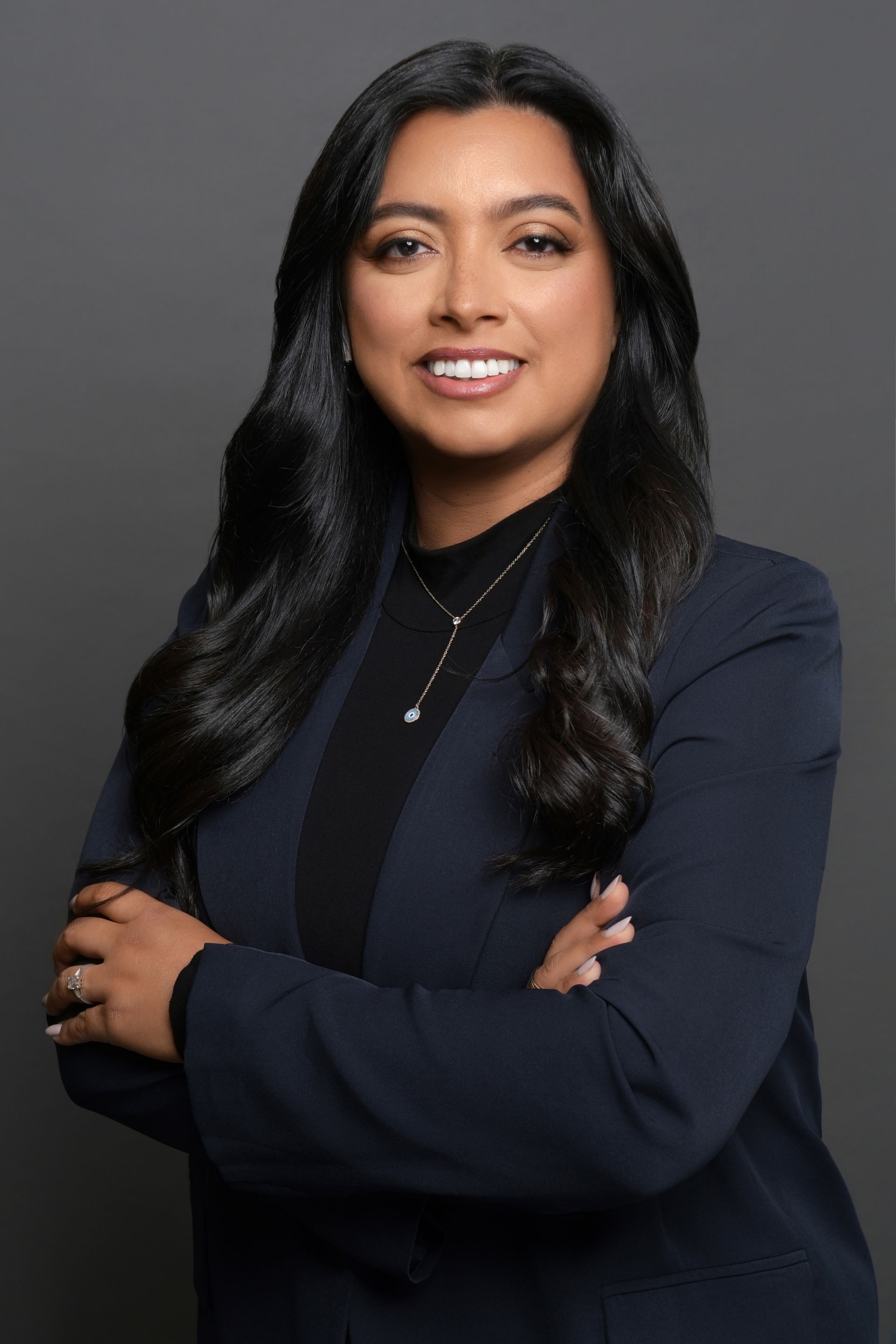 A woman in a blue jacket and black turtleneck is posing for a picture with her arms crossed.