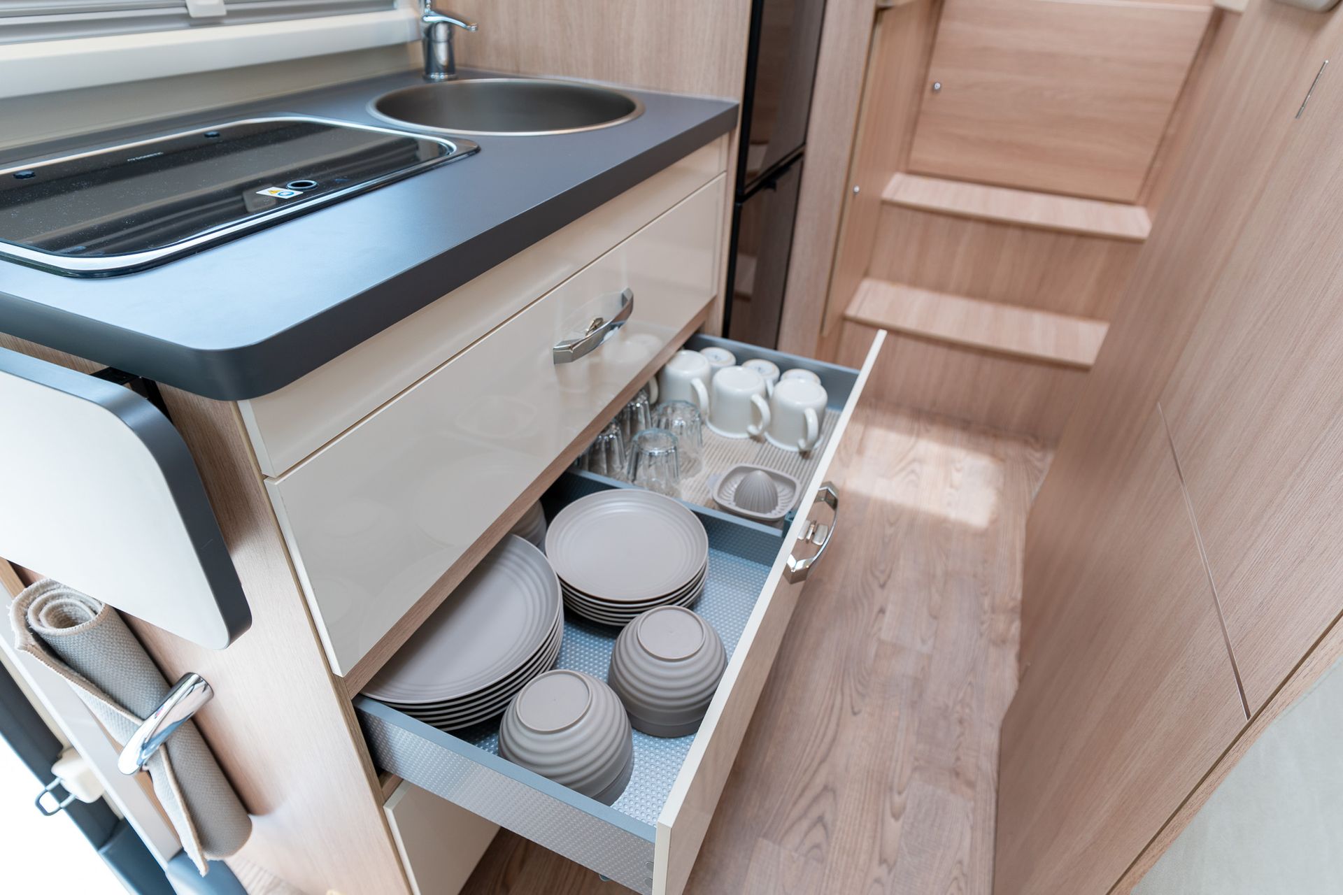 Una cocina en una caravana con un cajón lleno de platos y tazas.
