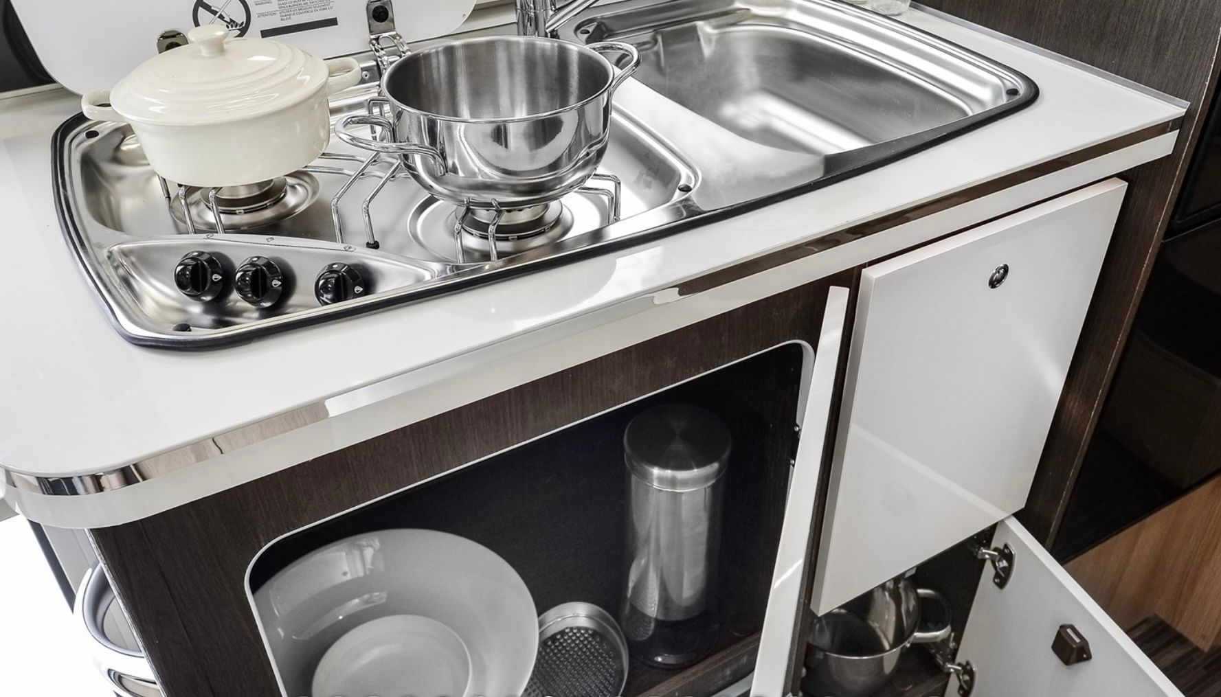 Una cocina con un fregadero, una estufa, ollas y sartenes.