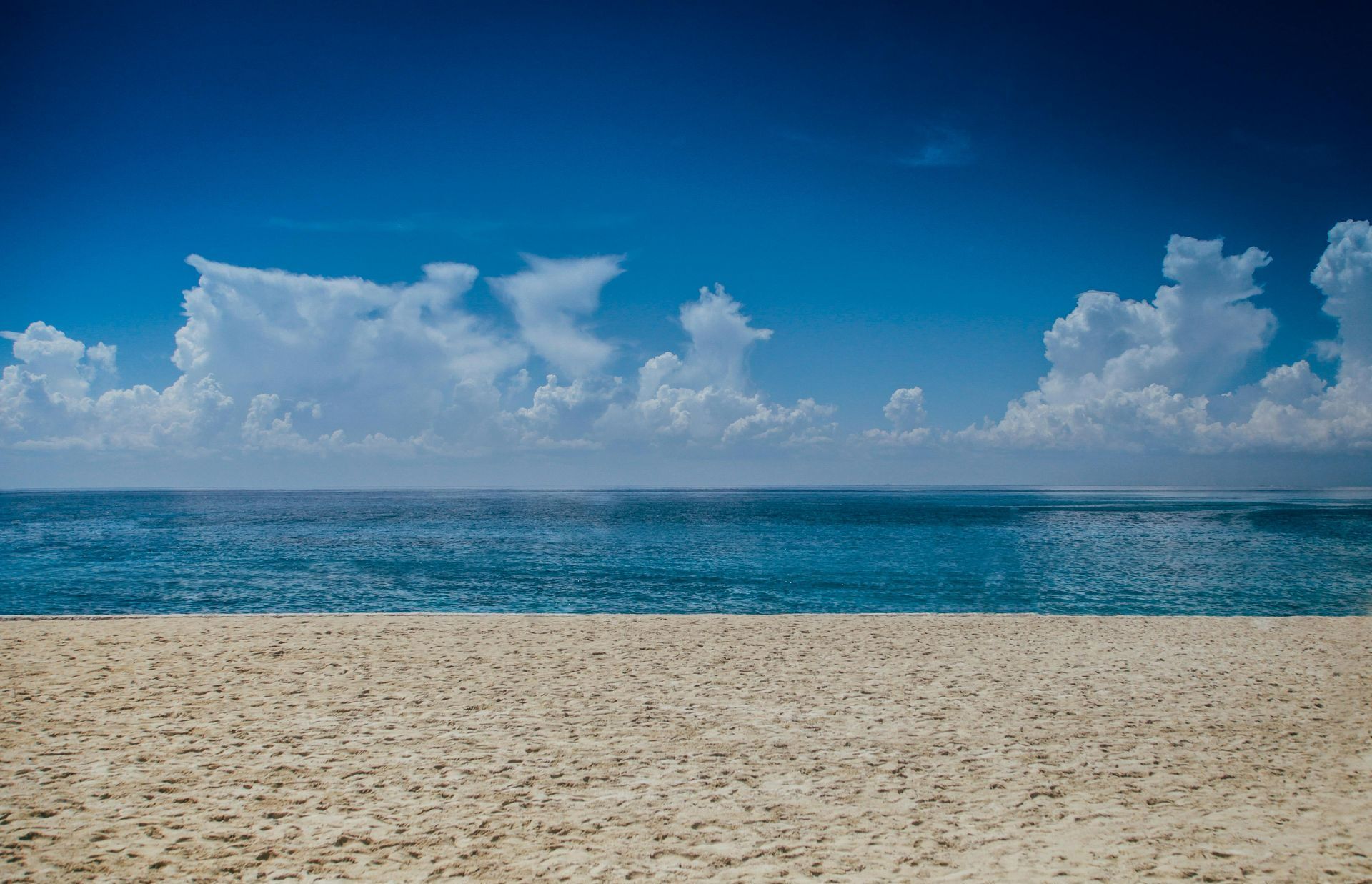 Una playa vacía con el océano al fondo y un cielo azul con nubes.