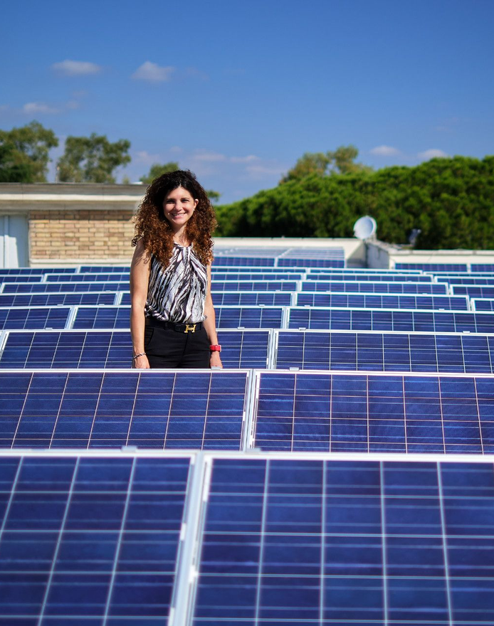 Una donna è in piedi davanti ai pannelli solari su un tetto. Cielo azzurro, giornata di sole.