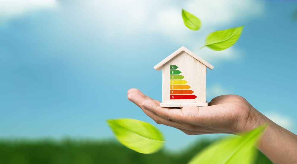 Mano che regge una casetta di legno in miniatura con classificazione energetica.