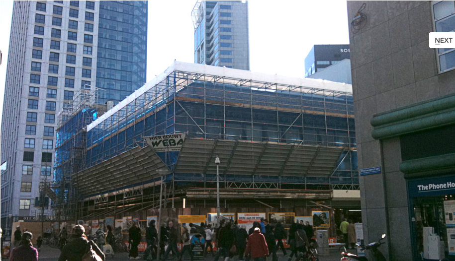 Een groep mensen loopt over straat, langs een gebouw in aanbouw.