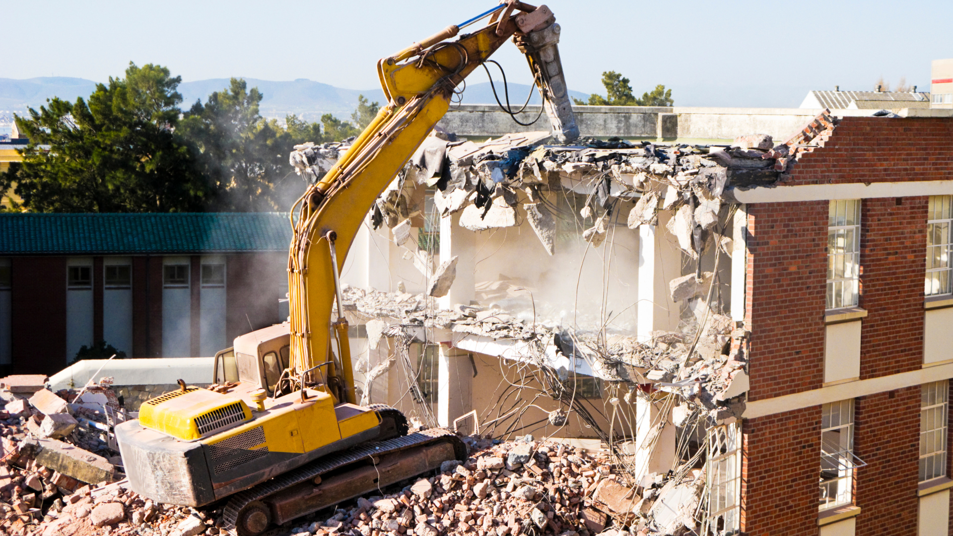A yellow excavator is demolishing a brick building