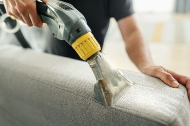 A man is cleaning a couch with a vacuum cleaner.