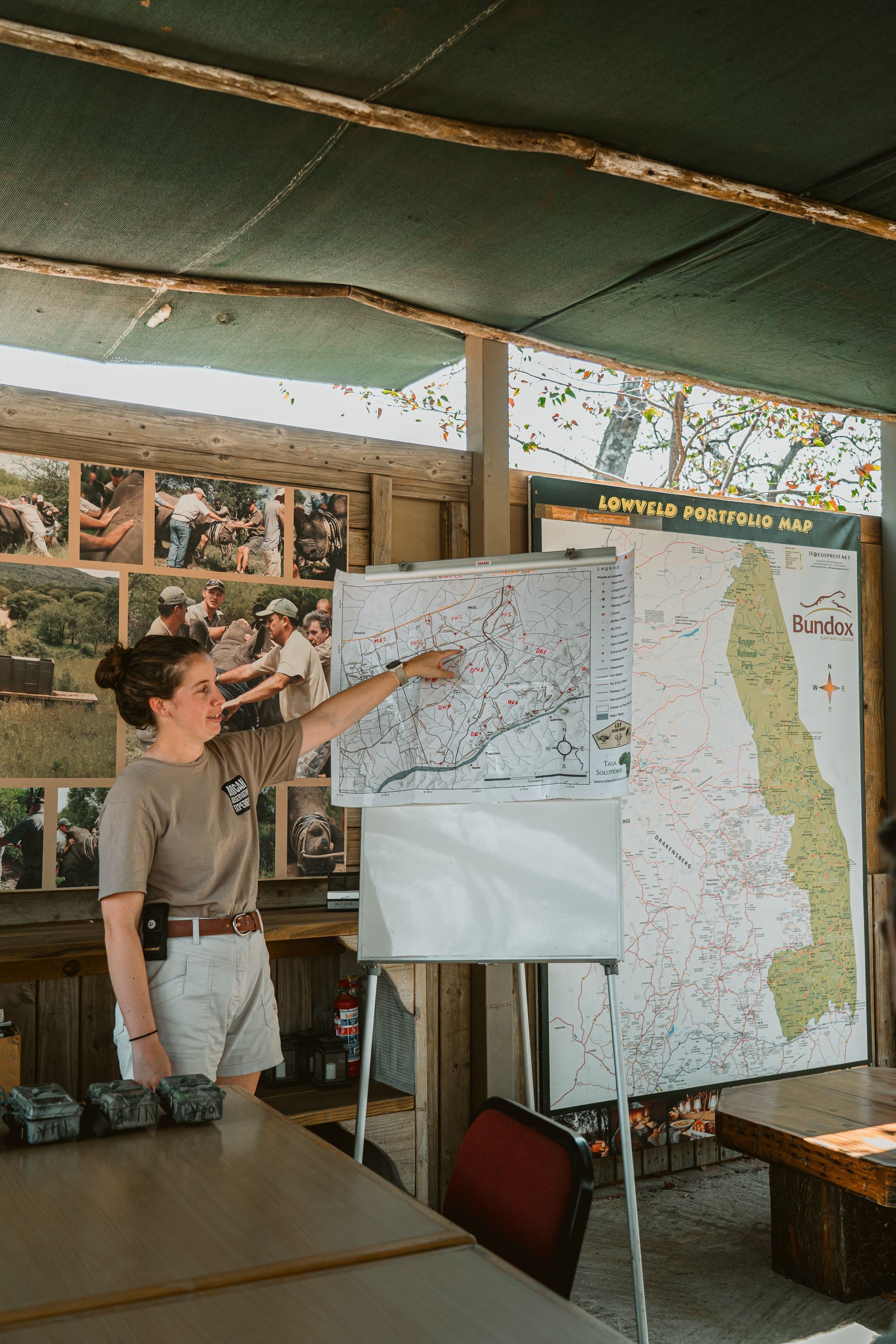 Woman pointing to a map on a whiteboard, explaining. Inside a rustic building.