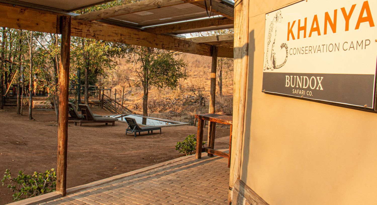 Khanya Conservation Camp entrance with a porch, lounge chairs, and wooded background.