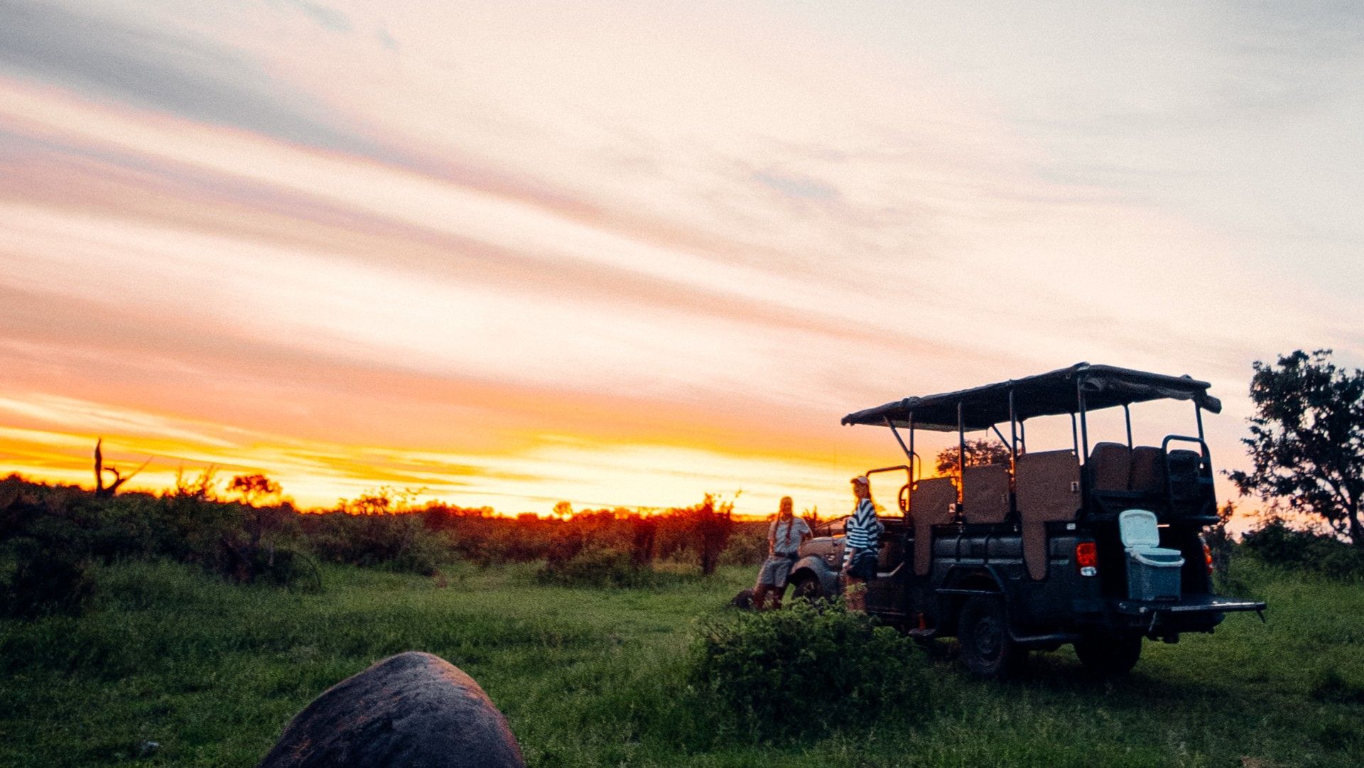 Sunset over grassy field with off-road vehicles and people silhouetted on the right