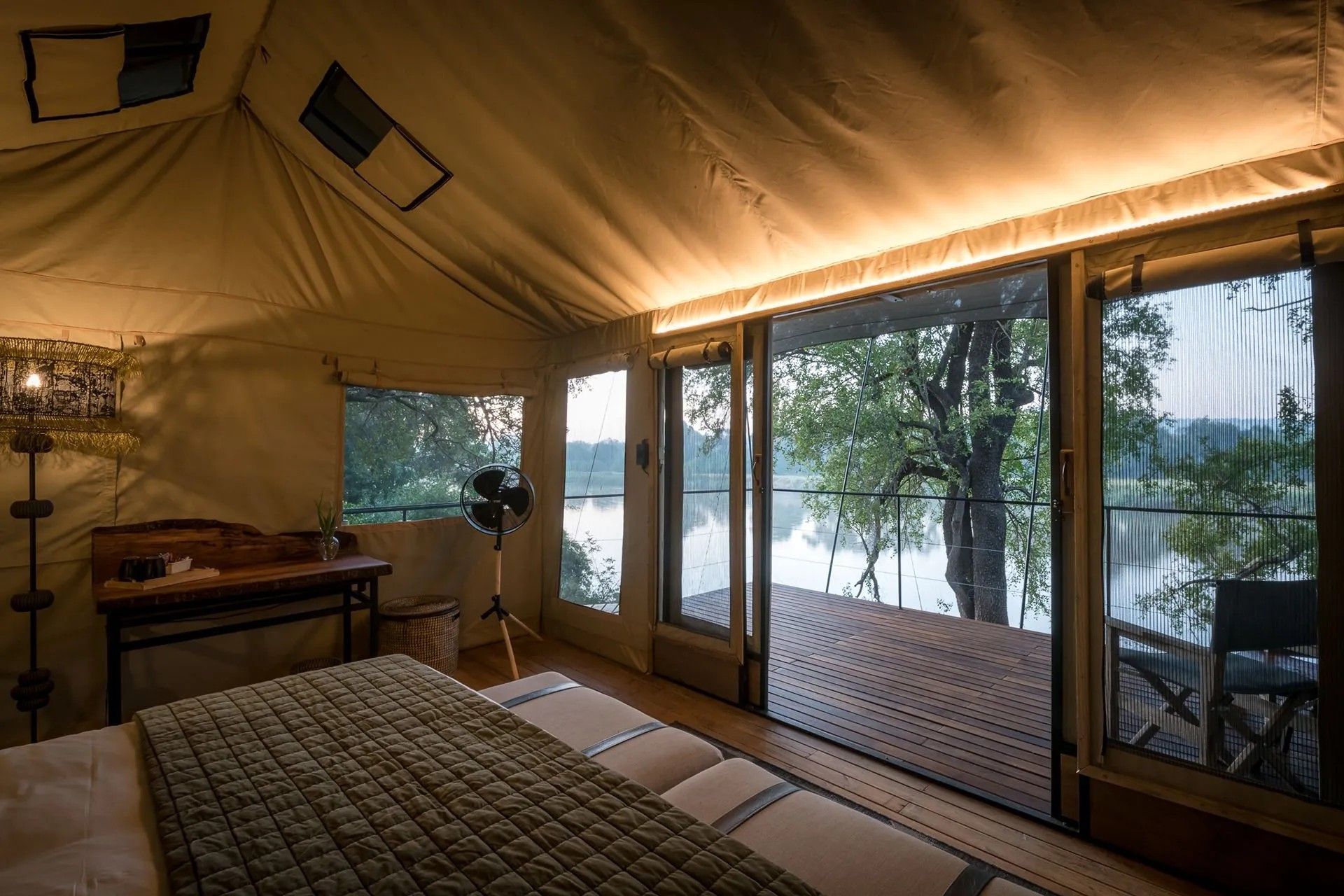 Interior of a canvas tent with a deck overlooking river. Bed, desk, and large windows.