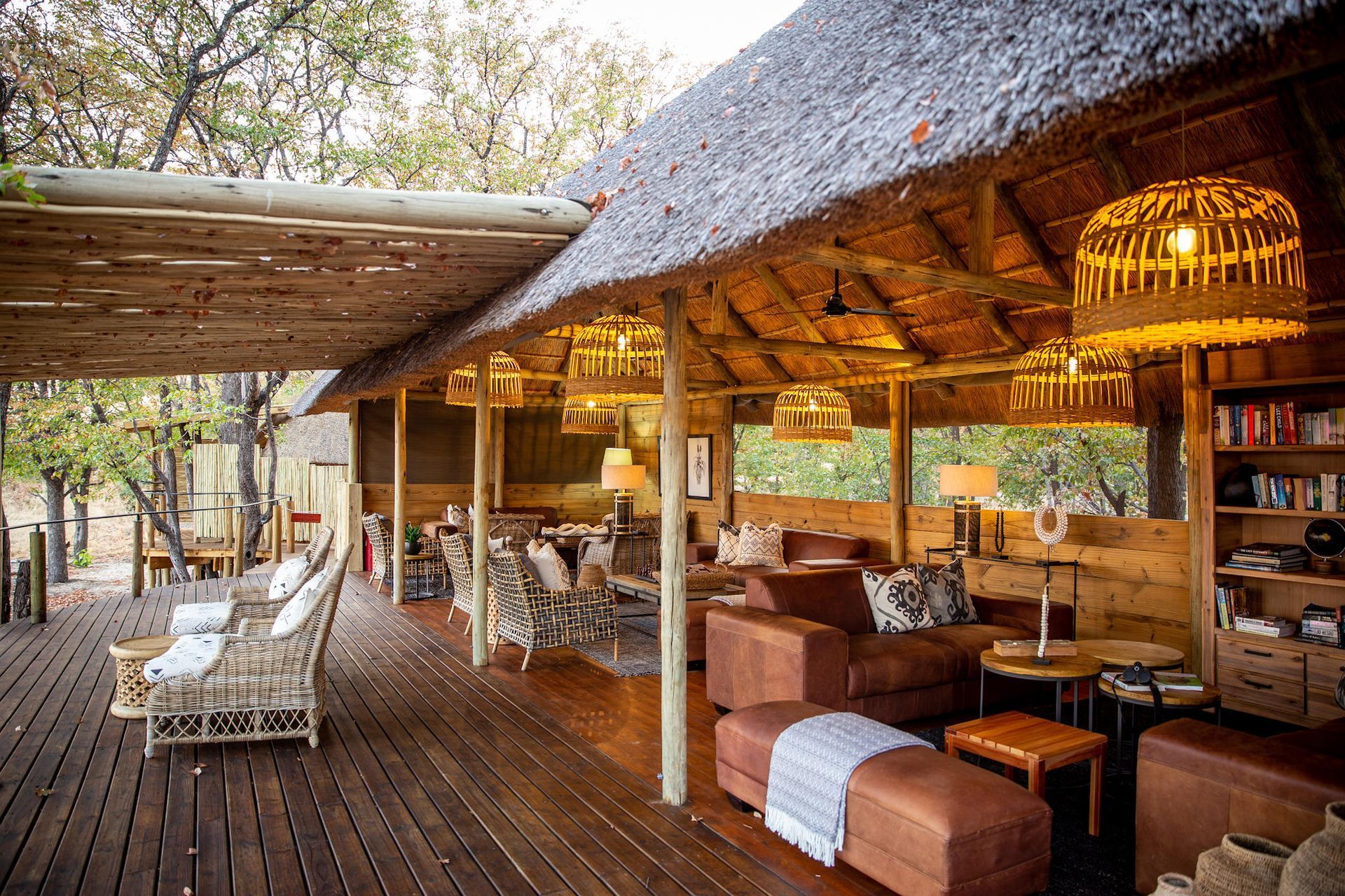 Outdoor lounge with thatched roof, wooden deck and cozy seating. Neutral tones, natural setting.