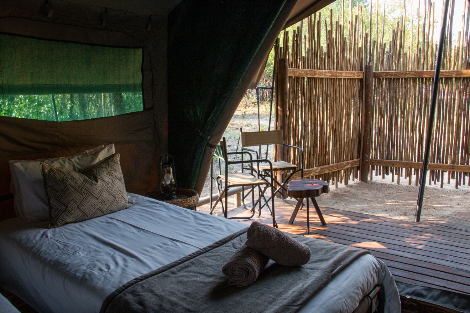 Safari-style tent bedroom with a bed, chair, and small table opening to a wooden deck outside