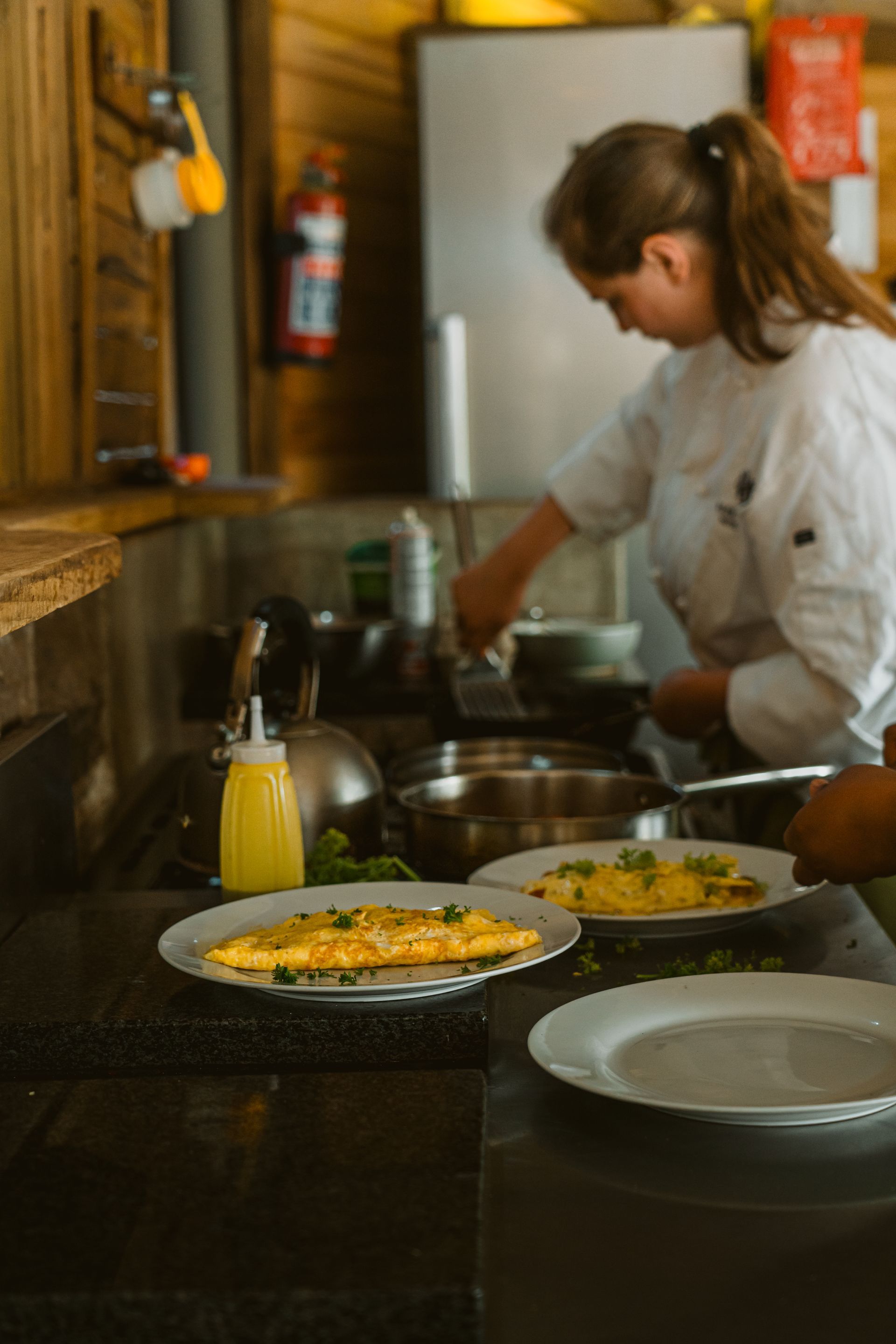 Chef preparing omelets in a commercial kitchen with finished plates in the foreground.