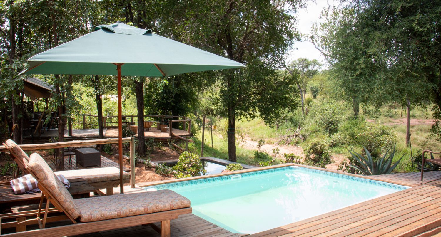 Interior of a luxury glamping tent with bed, desk, and large windows overlooking a deck and water.