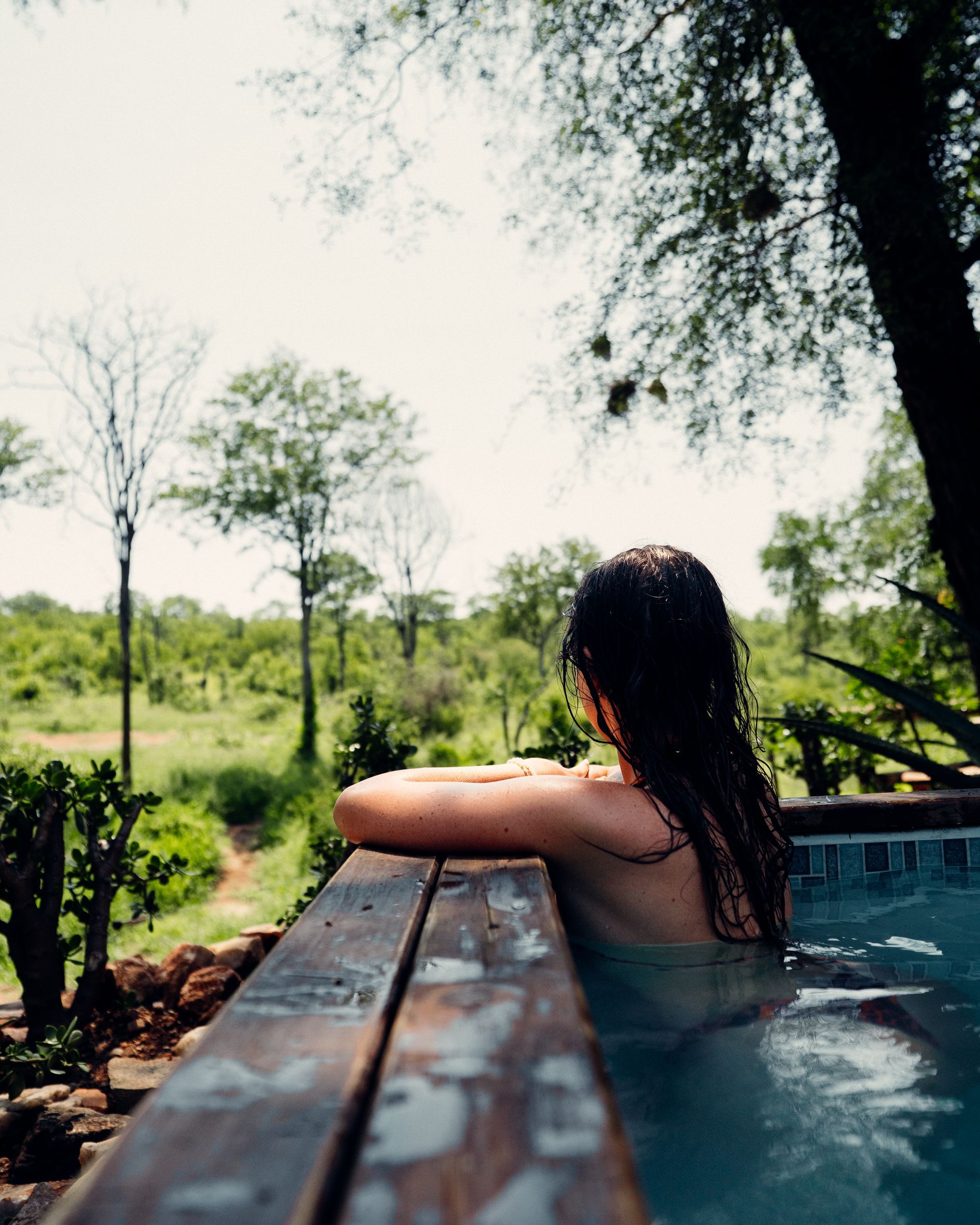 Person resting in a hot tub, looking over a wooden edge toward a sunny green landscape
