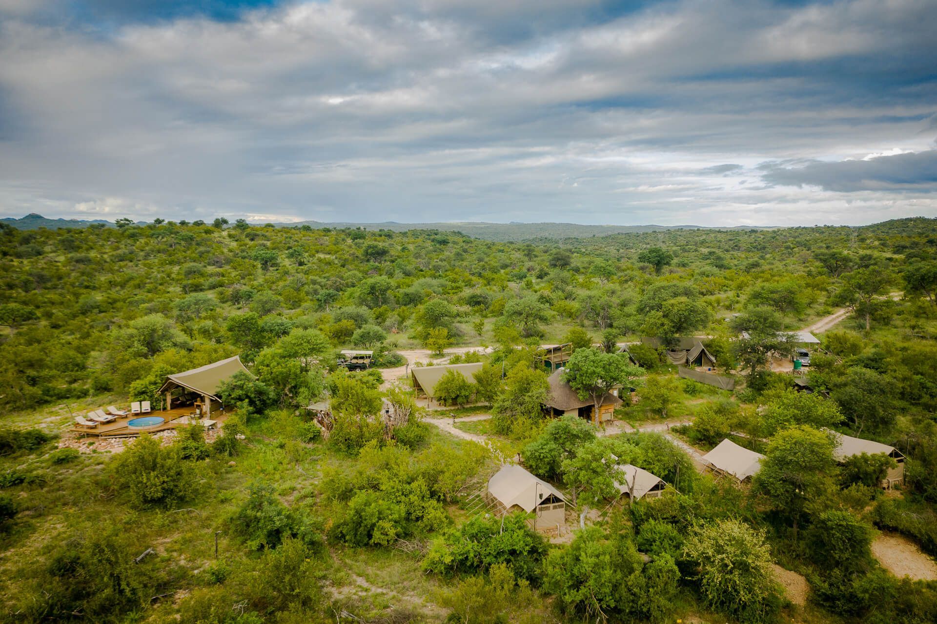 Aerial view of safari lodge in lush green savanna under cloudy sky.