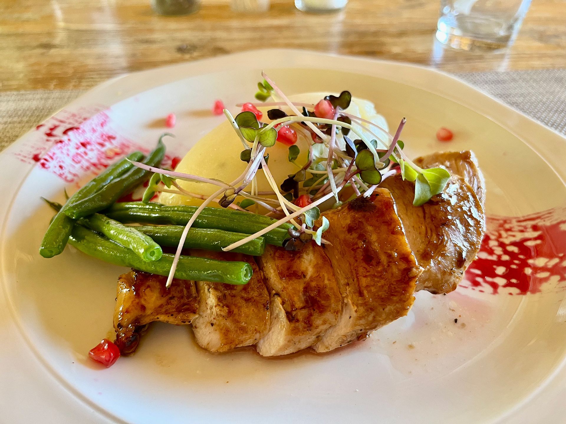 Sliced grilled meat with green beans, mashed potatoes, and garnishes on a white plate.