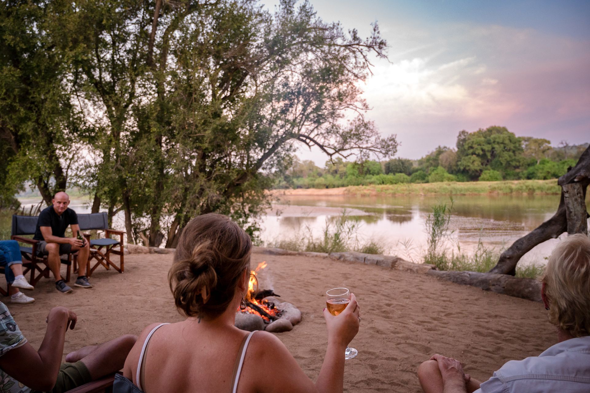 Bundox guests around a firepit, enjoying a sundowner overlooking a the Olifants river at dusk.