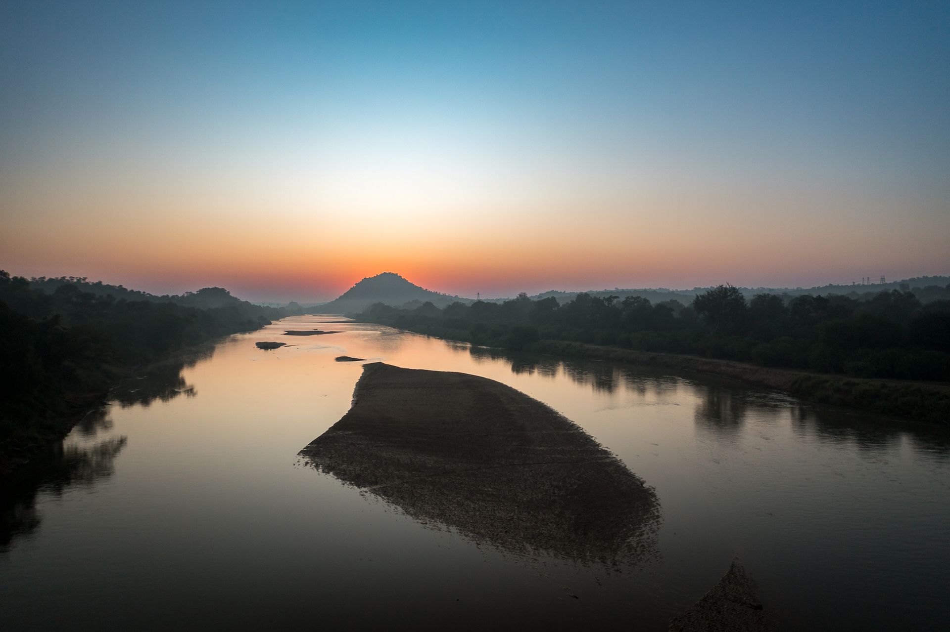Sunrise over the Olifant river with a central island and trees on the banks; soft colors of orange, blue, and gray.