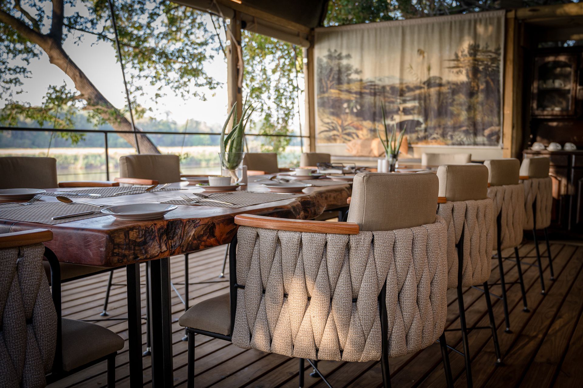 Long dining table set for a meal outdoors, chairs with woven backs, Olifants river view.