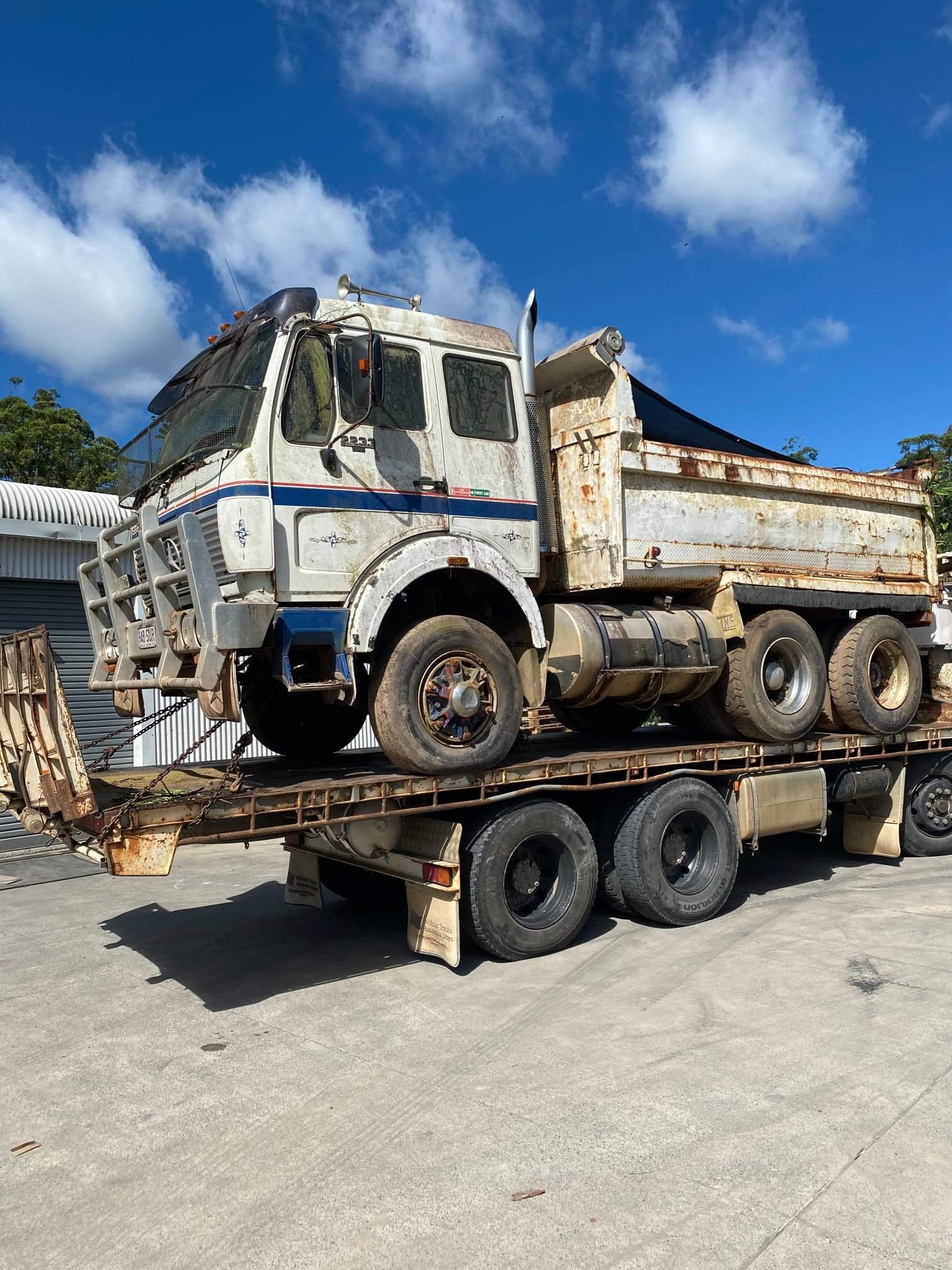 A Dilapidated White And Blue Dump Truck On A Flatbed Trailer Under A Blue Sky — H&H Metal Recycling in Kenilworth, QLD