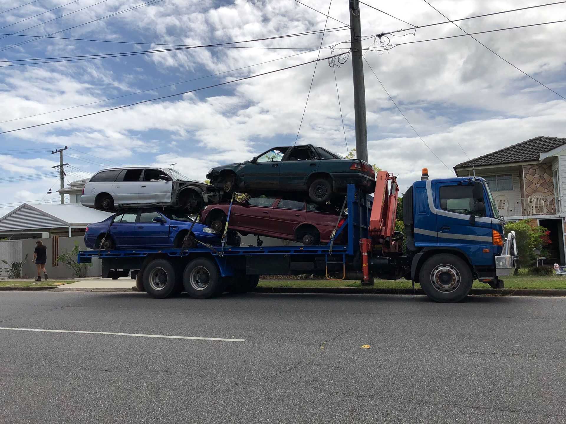 A Tow Truck Carrying Five Wrecked Cars On A Residential Street — H&H Metal Recycling in Bells Creek, QLD