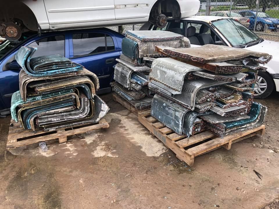 Stacks Of Car Parts On Pallets At A Junkyard, With Discarded Vehicles — H&H Metal Recycling in Moffat Beach, QLD