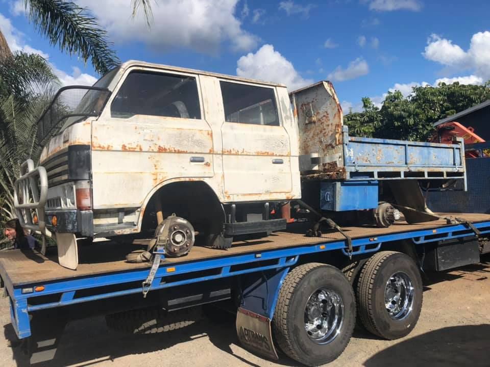 Rusty White Truck Cab On A Blue Flatbed Trailer, Tires Missing. Bright Sunny Day — H&H Metal Recycling in Beerwah, QLD