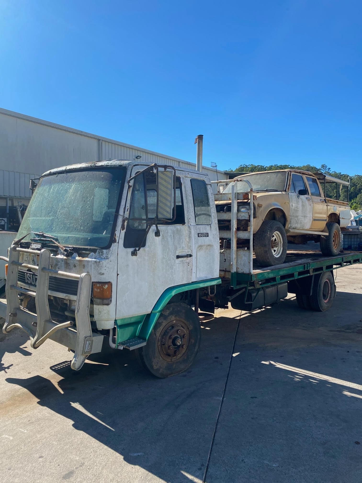 White Truck With A Flatbed Carrying A Beige Suv On A Sunny Day — H&H Metal Recycling in Gympie, QLD