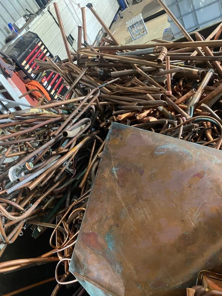 A Pile of Copper Pipes and a Large Copper Sheet Are in a Cluttered Workshop