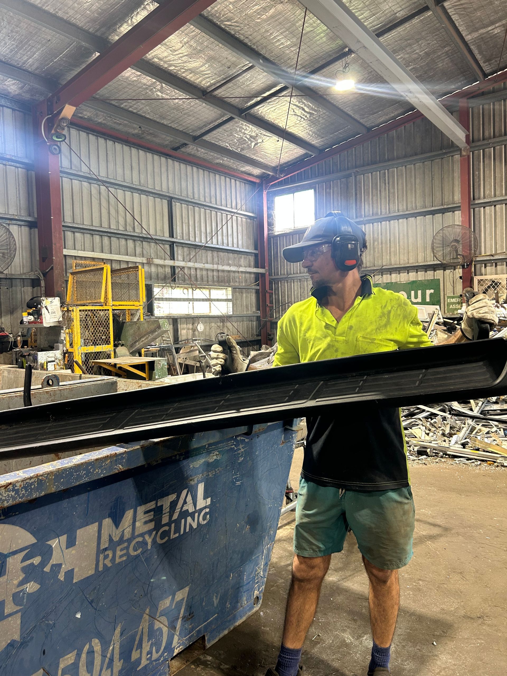 Worker Holding a Long Black Metal Piece Over a Recycling Bin— H & H Metal Recycling In Maroochydore, QLD