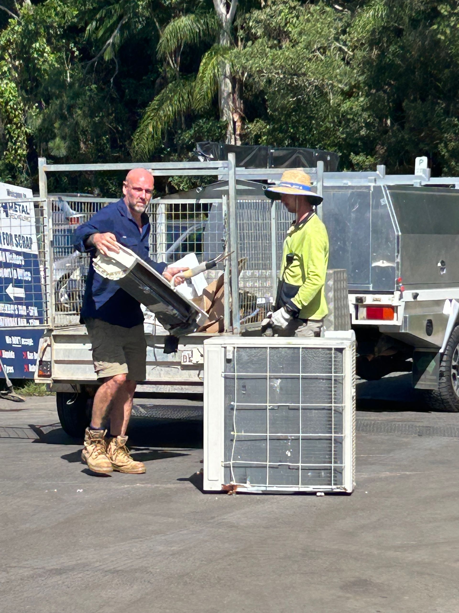 Two Workers in a Parking Lot Loading an Outdoor Air Conditioning Unit — H&H Metal Recycling in Caloundra West, QLD
