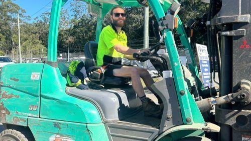 A Man Is Sitting in A Green Forklift — H & H Metal Recycling In Warana, QLD