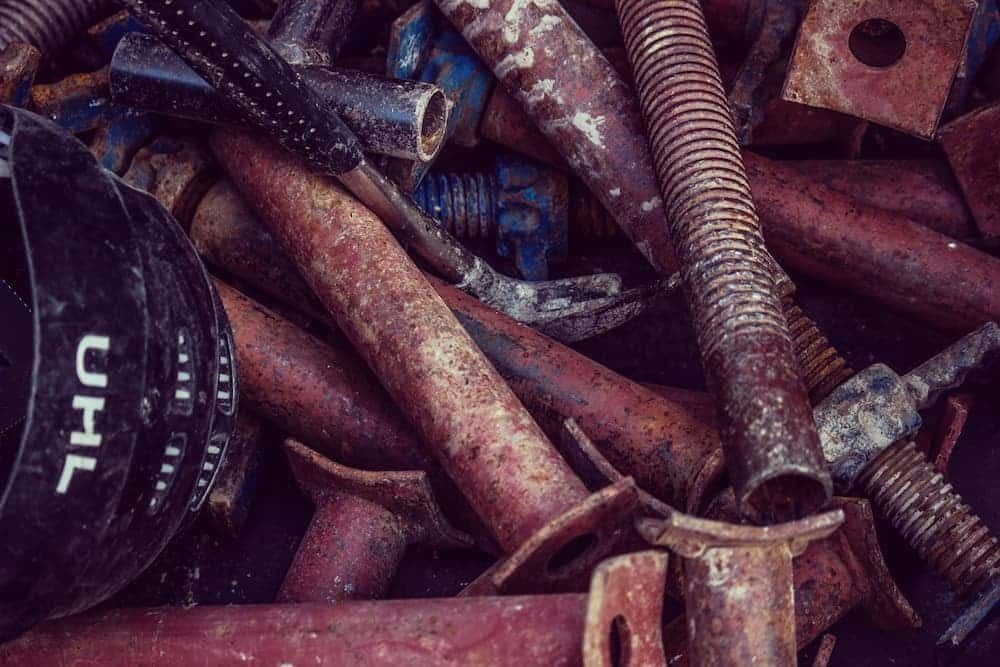 Close-up of rusty metal pipes, bolts, and fittings mixed with a black plastic object.